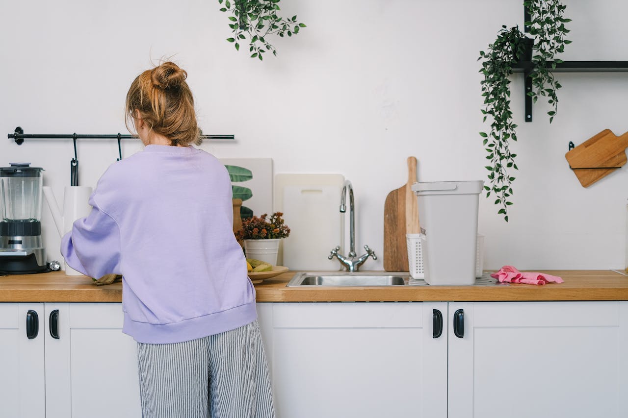 services-03 Back view of unrecognizable young female in casual clothes standing at wooden counter in light kitchen in daytime